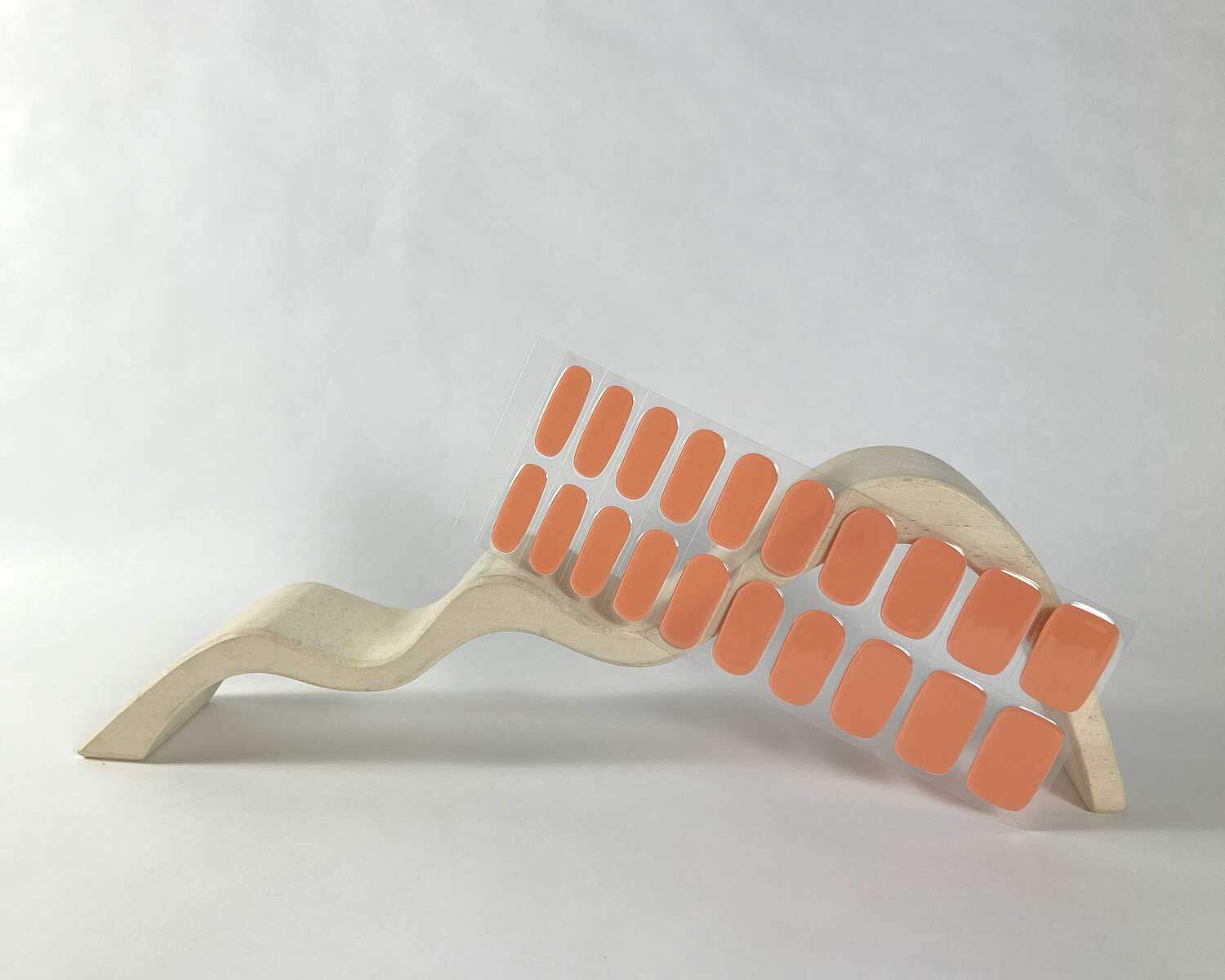 Classic coral orange semi-cured gel nails in mockup to show product against white wave wooden block