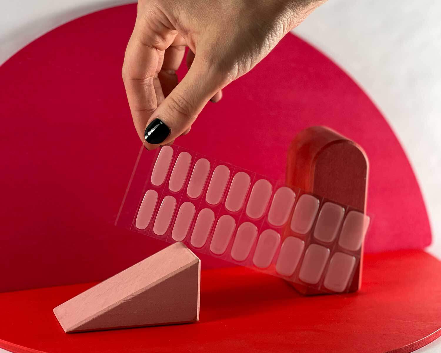 Soft pink semi-cured gel nails in mockup to show product against red wooden blocks with hand holding strip