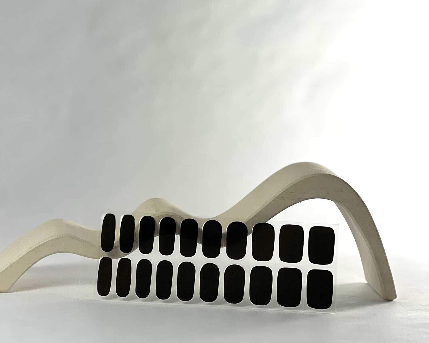 Night black semi-cured gel nails in mockup to show product against white wave wooden block with la-bek uv lamp in the background