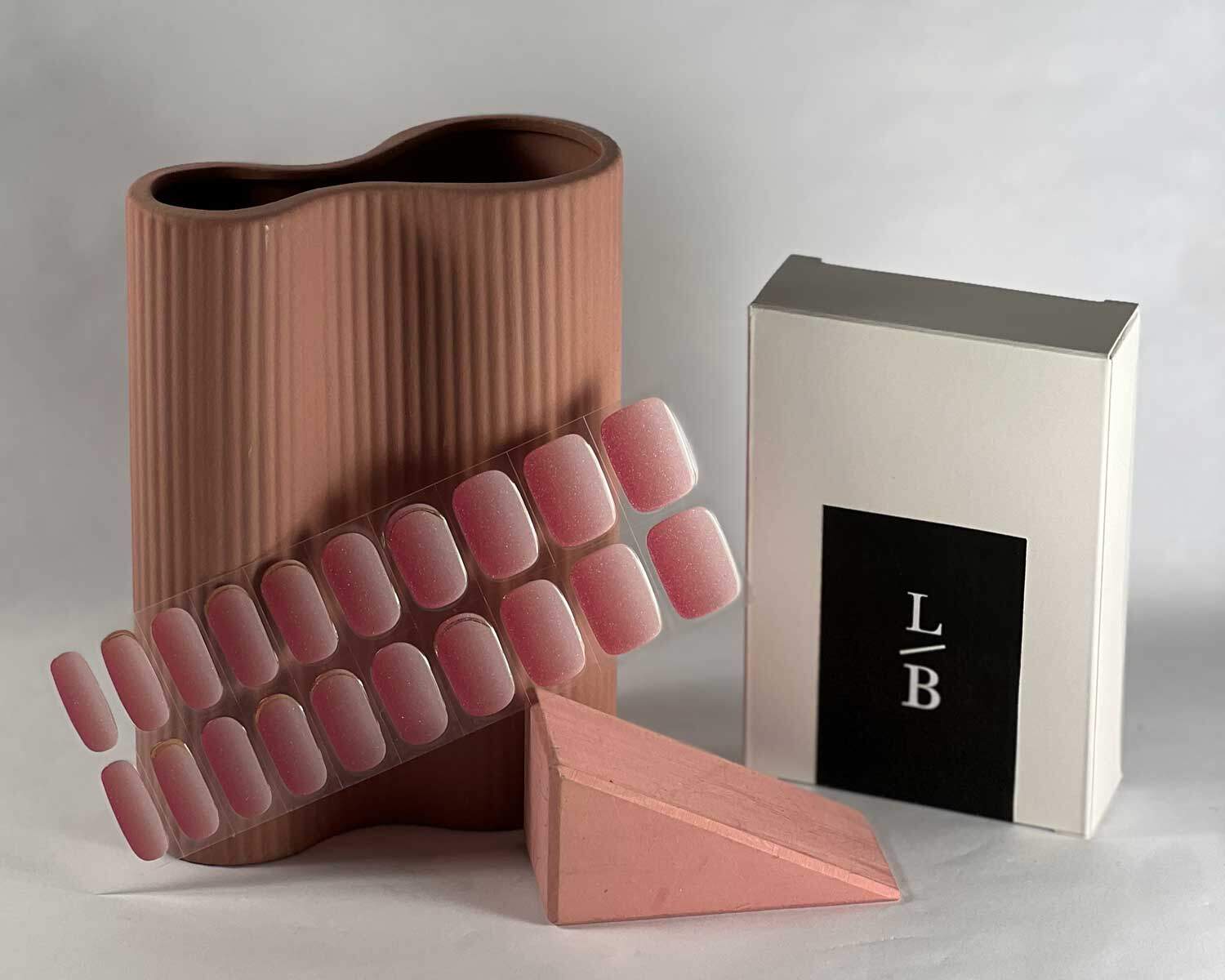 Golden sunset pink semi-cured gel nails in mockup to show product against wooden block and peach vase with la-bek uv lamp in the background