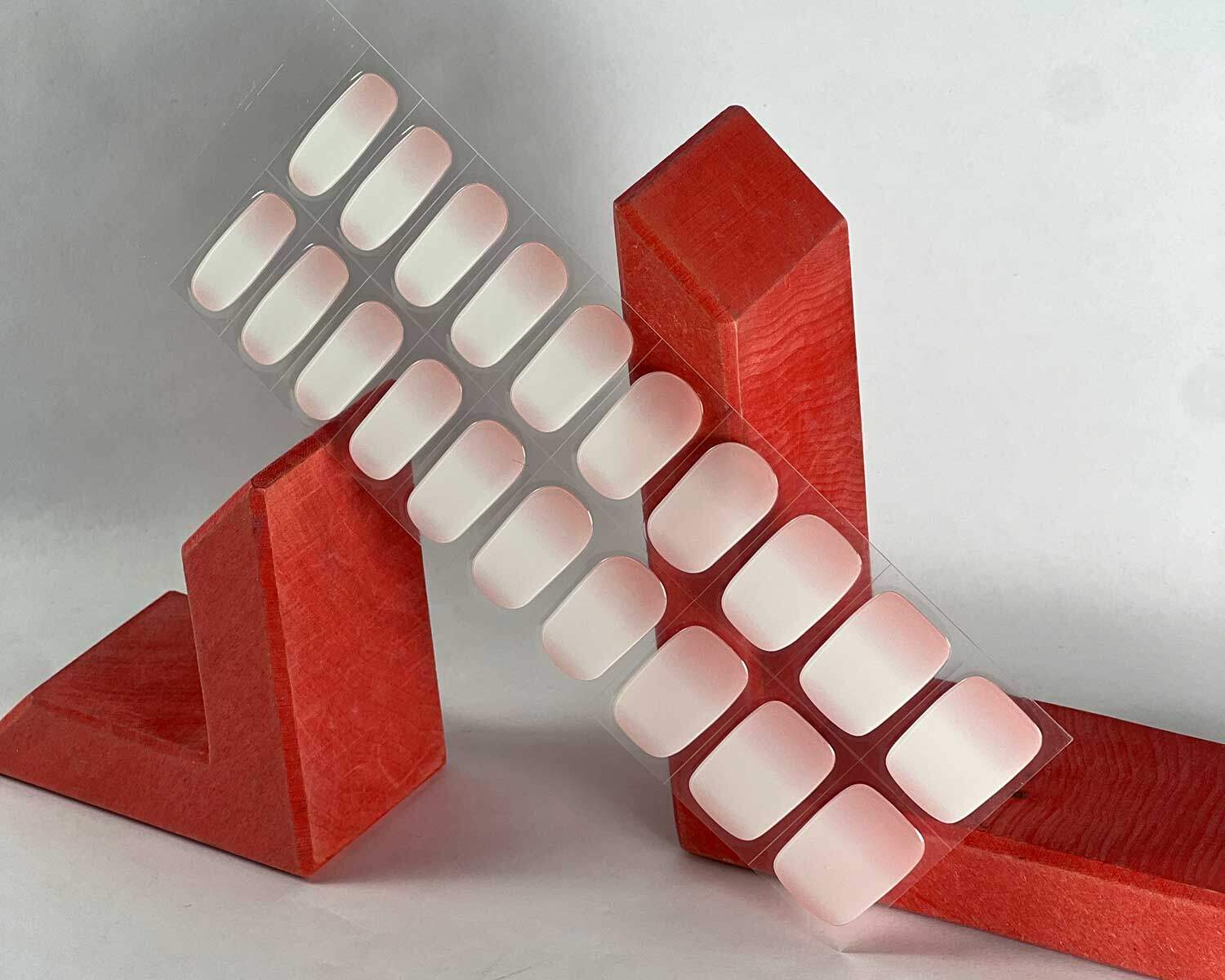 Ombre pink semi-cured gel nails in mockup to show product against red wooden blocks with la-bek uv lamp in the background