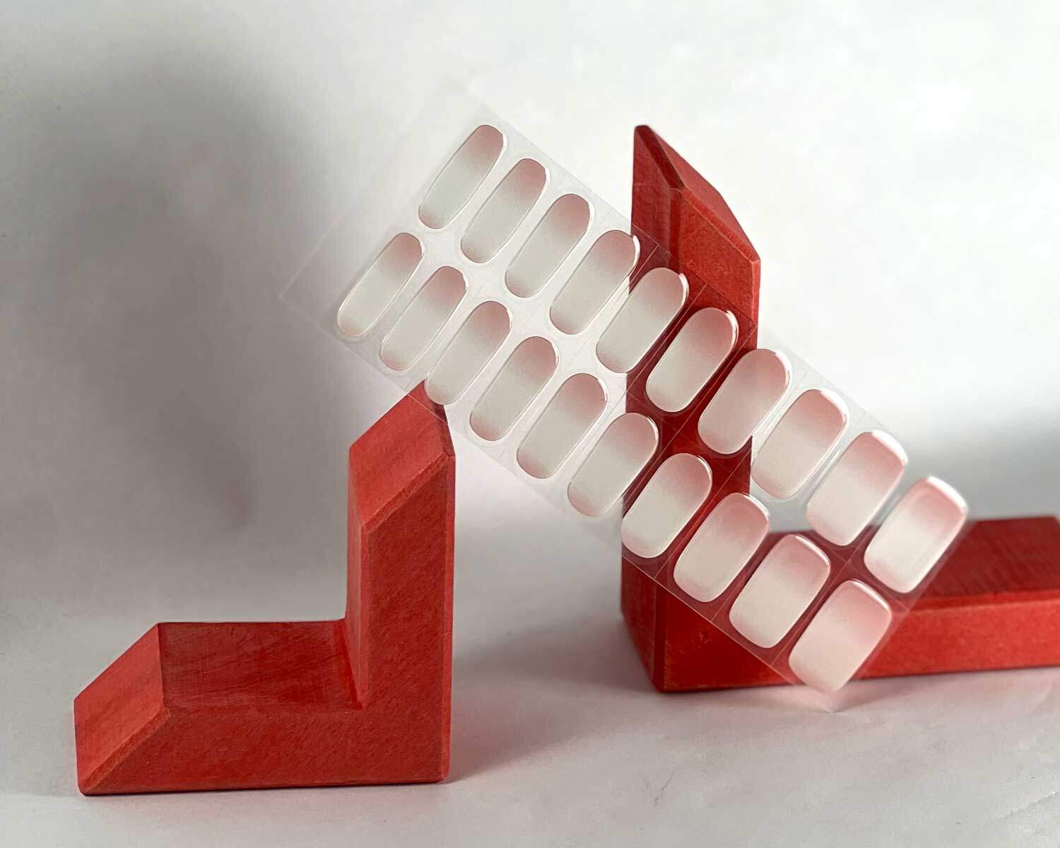 Ombre pink semi-cured gel nails in mockup to show product against red wooden blocks with la-bek uv lamp in the background