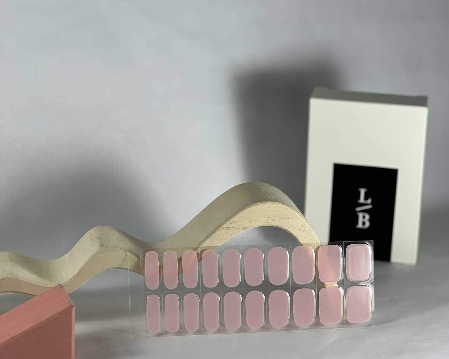 Pale pink power semi-cured gel nails in mockup to show product against white wave and pink wooden blocks with la-bek uv lamp in the background