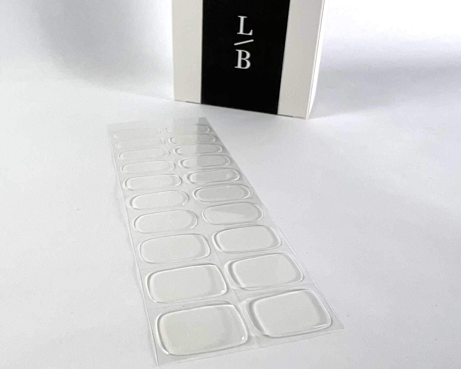 Transparent clear semi-cured gel nails on angle zoomed in on white background with la-bek uv lamp box in the background