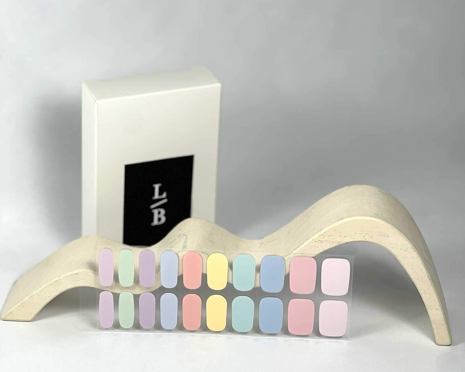 Candy bar rainbow semi-cured gel nails in mockup to show product against white wave wooden blocks with la-bek uv lamp in the background