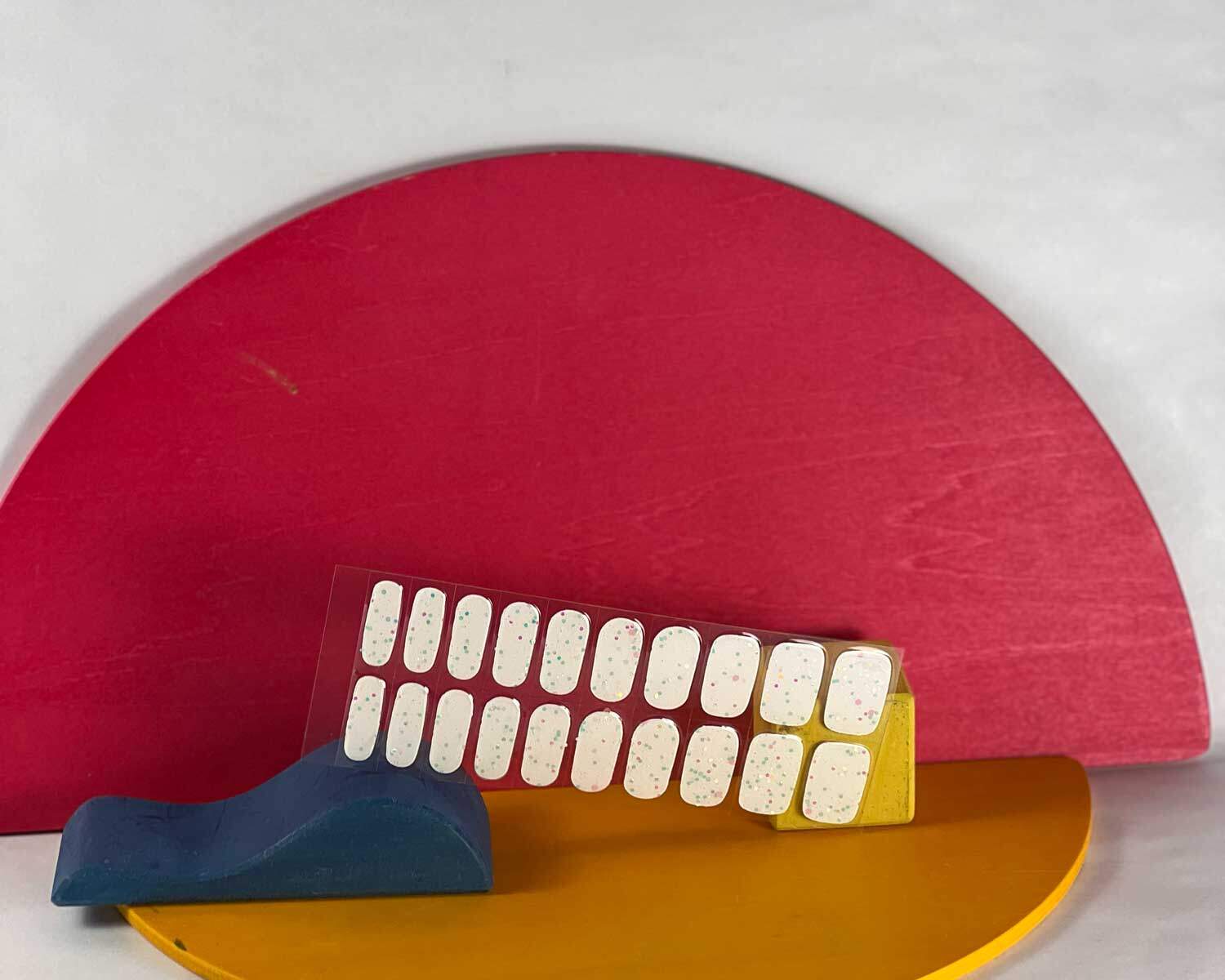 Sprinkle-Glow-Snow-semi-cured-gel-nail-mock2 Sprinkle snow Glow in the dark white semi-cured gel nails in mockup to show product against blue, red and yellow wooden blocks