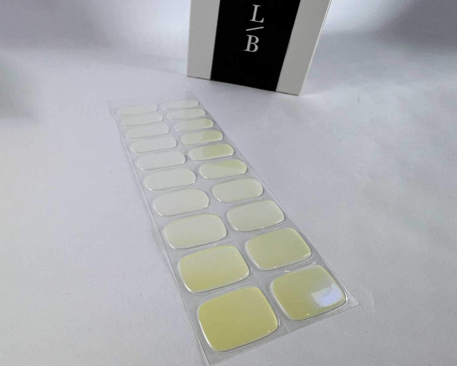 Pearlescent Lemon yellow blue semi-cured gel nails on angle zoomed in on white background with la-bek uv lamp box in the background