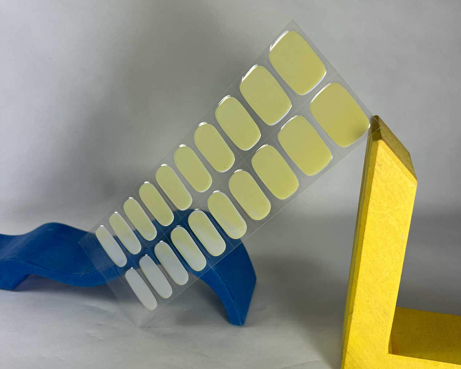 Pearlescent Lemon yellow blue semi-cured gel nails in mockup to show product against yellow and blue wave wooden blocks