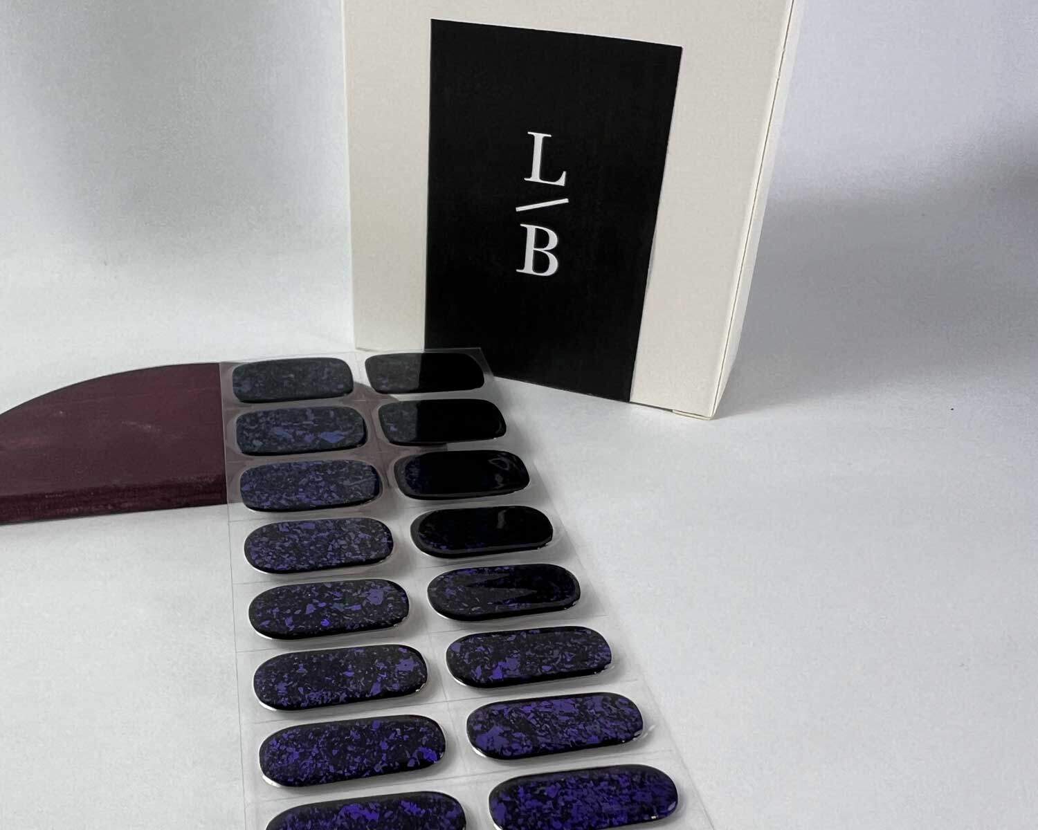 Violet Luster black and purple semi-cured gel nails on angle zoomed in on white background with la-bek uv lamp box in the background