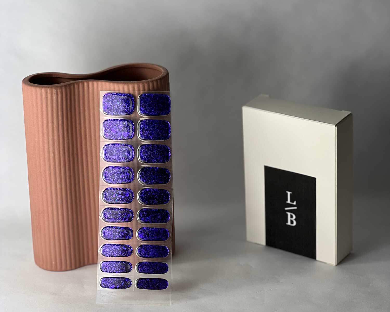 Violet Luster black and purple semi-cured gel nails in mockup to show product against peach vase with la-bek uv lamp in the background