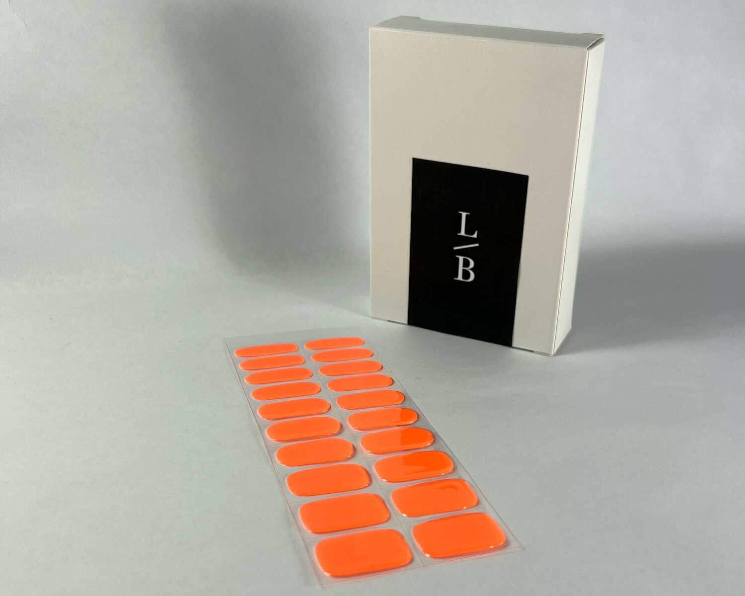 Neon Orange Glow in the dark semi-cured gel nails on angle zoomed in on white background with la-bek uv lamp box in the background