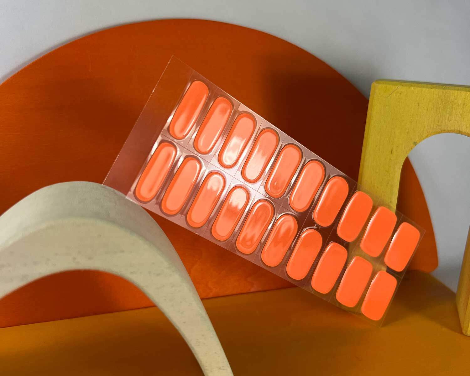 Neon Orange Glow in the dark semi-cured gel nails in mockup to show product against white, orange and yellow wooden blocks