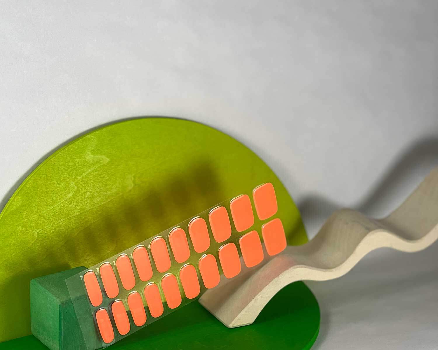 Neon Orange Glow in the dark semi-cured gel nails in mockup to show product against green and white wooden blocks