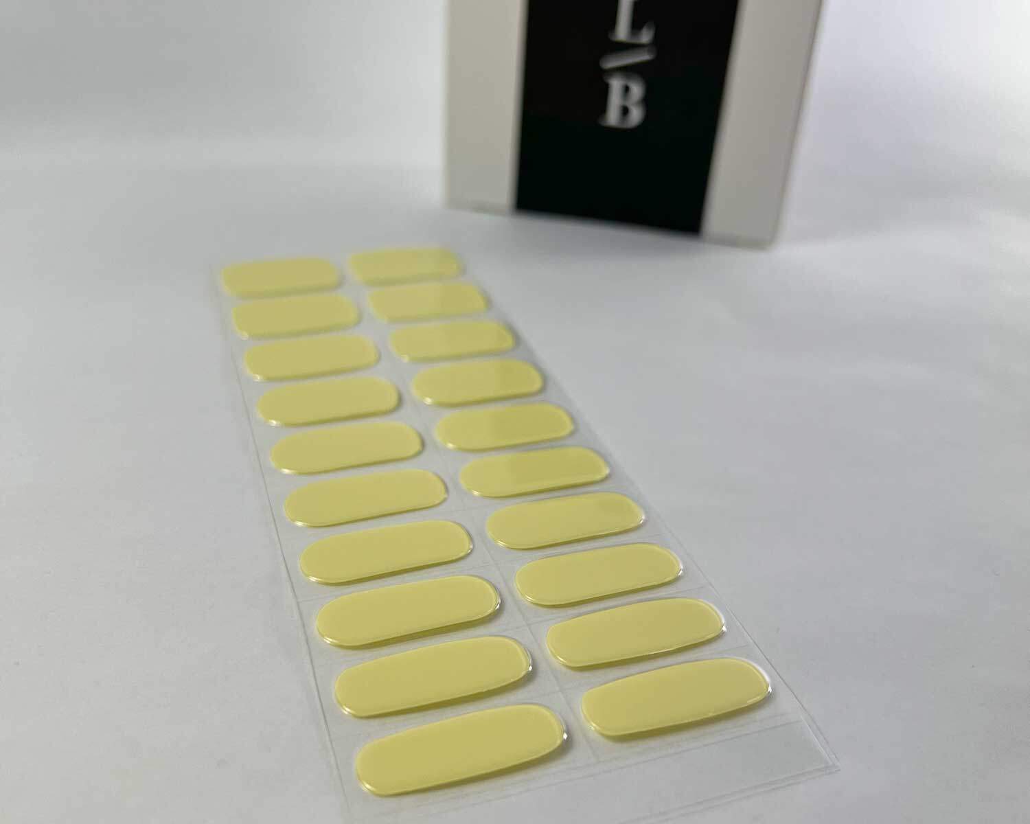 Lemonade yellow semi-cured gel nails on angle zoomed in on white background with la-bek uv lamp box in the background