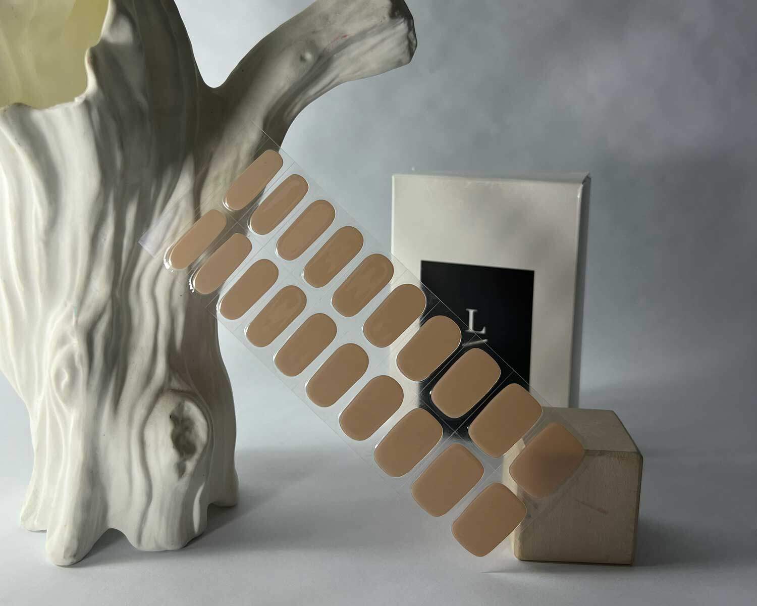 oat latte brown semi cured gel nails in mockup to show product against wooden block and white tree with la-bek uv lamp in the background